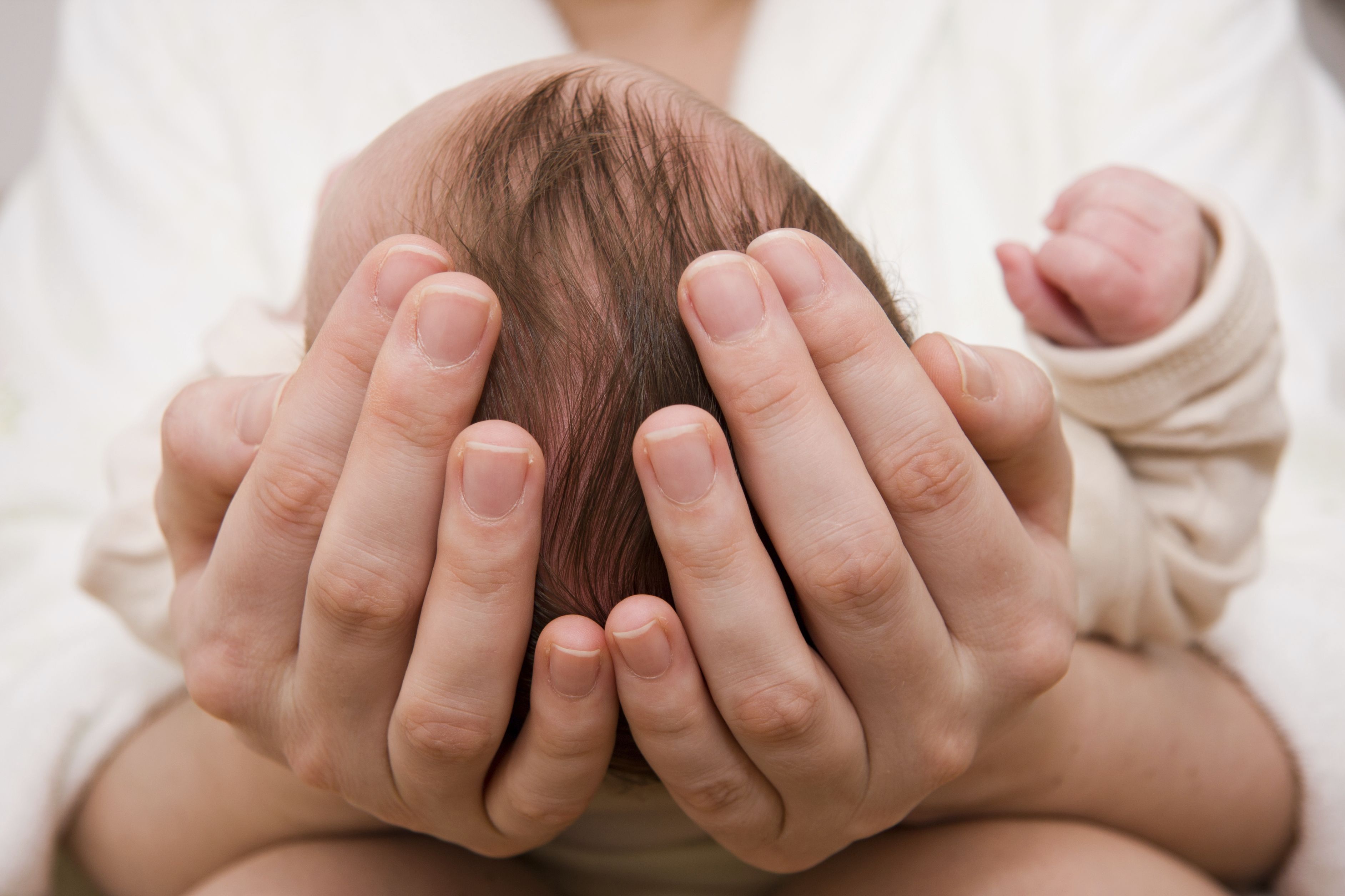 Eine sanfte Hand hält den Kopf eines neugeborenen Babys, während die andere Hand des Elternteils bereit ist, zu helfen.