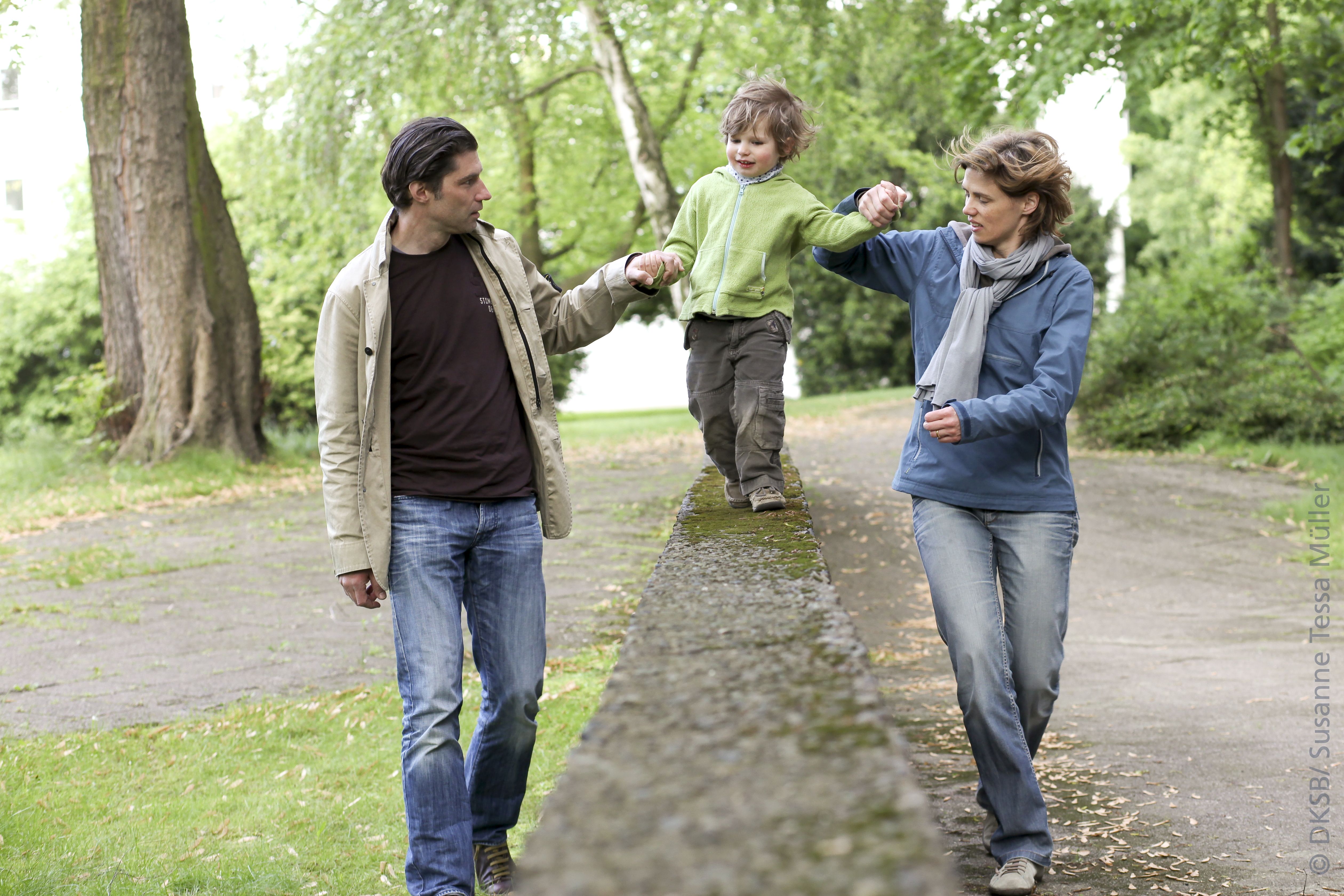 Ein Junge balanciert auf einer Mauer, während seine Eltern ihn sicher halten und ihn anfeuern.