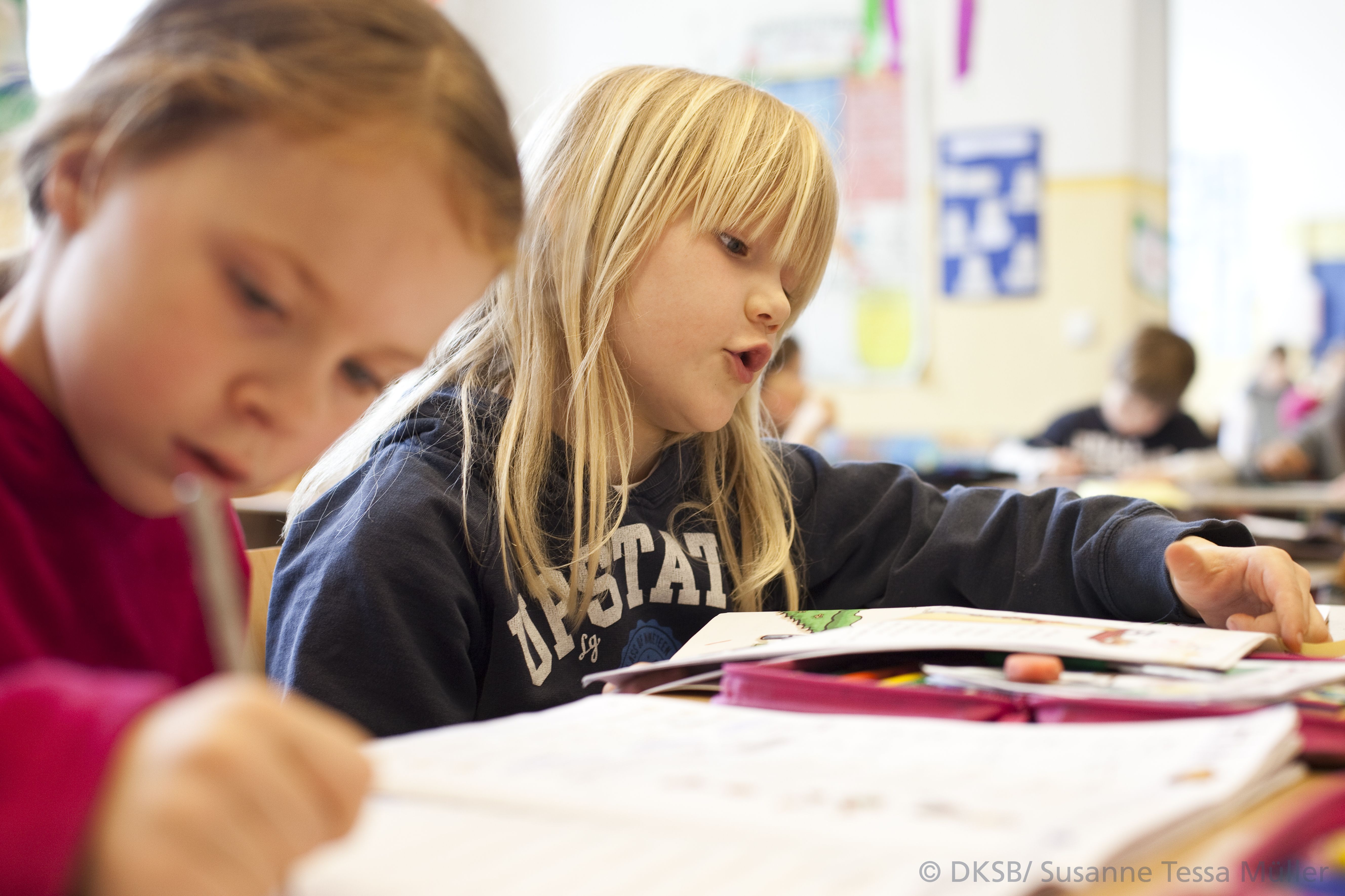 Zwei Mädchen arbeiten in einem Klassenzimmer an ihren Schulaufgaben, während sie konzentriert zeichnen und lesen.